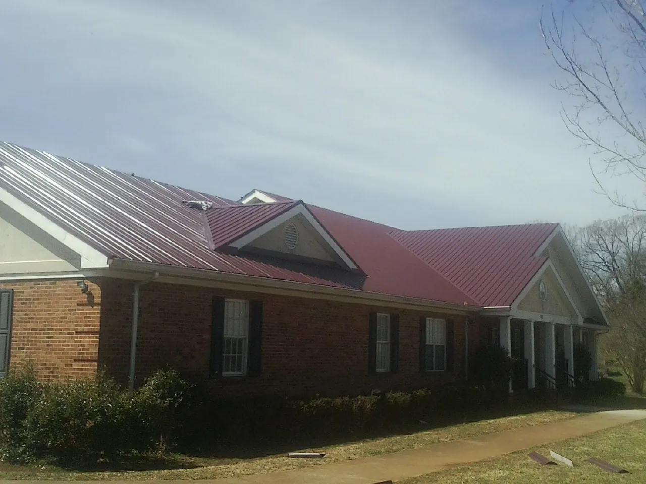 Red metal roof with gabled entries on a long brick building, from a Hail Damage Roof Repair job in Fort Myers Beach