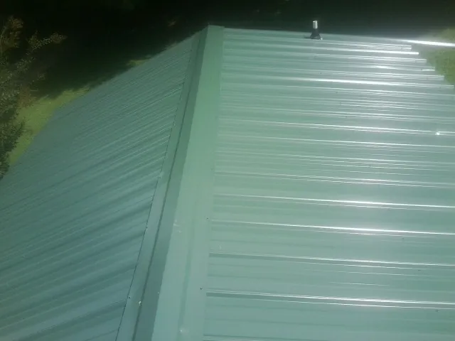 New green metal panels meeting at the ridge of a roof — Flat Roof Repair work by our crew in Fort Myers Beach