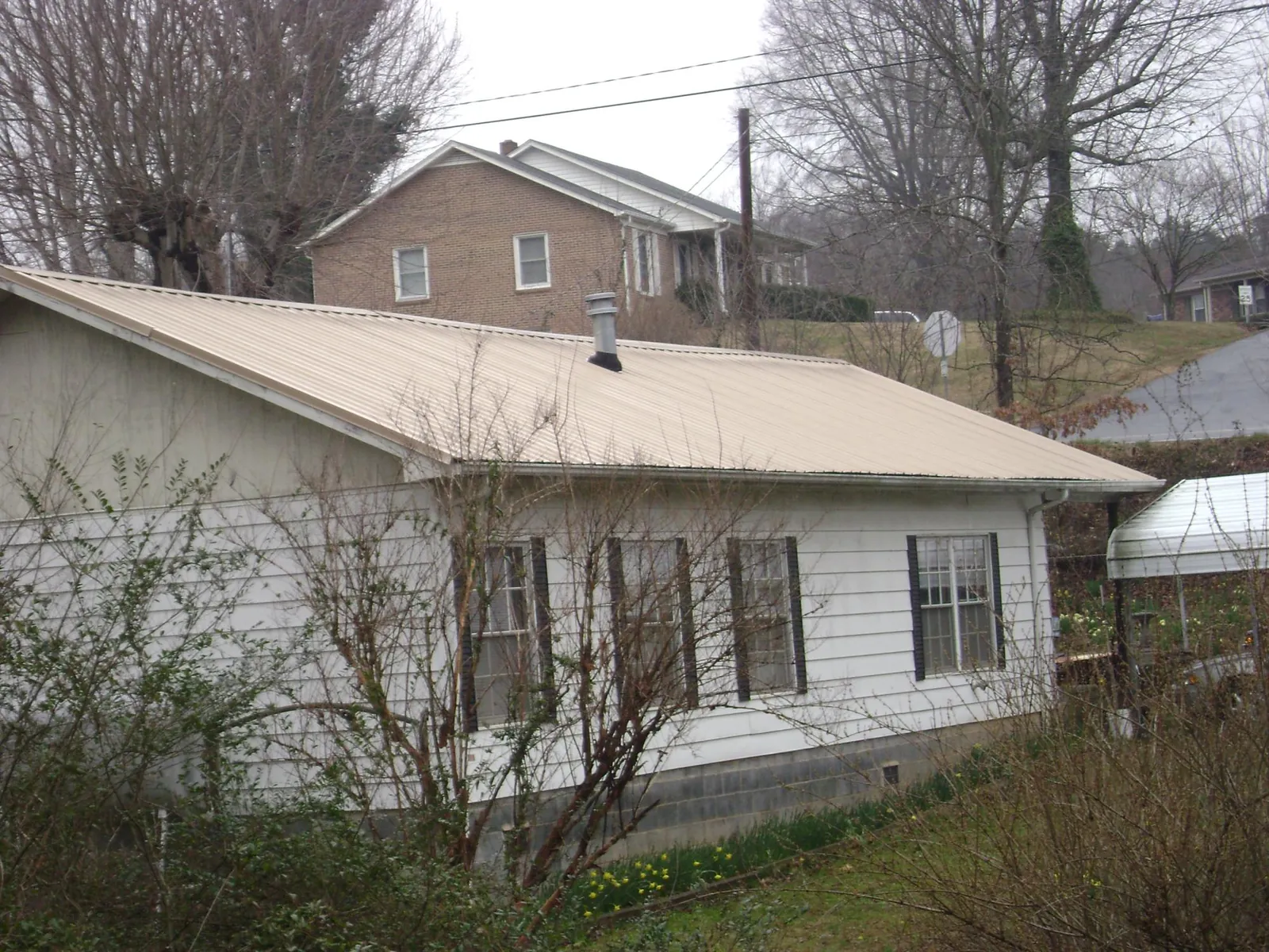 Tan metal roof on a white sided house set into a hillside — Commercial Roofing by Roofing Brothers in Fort Myers Beach